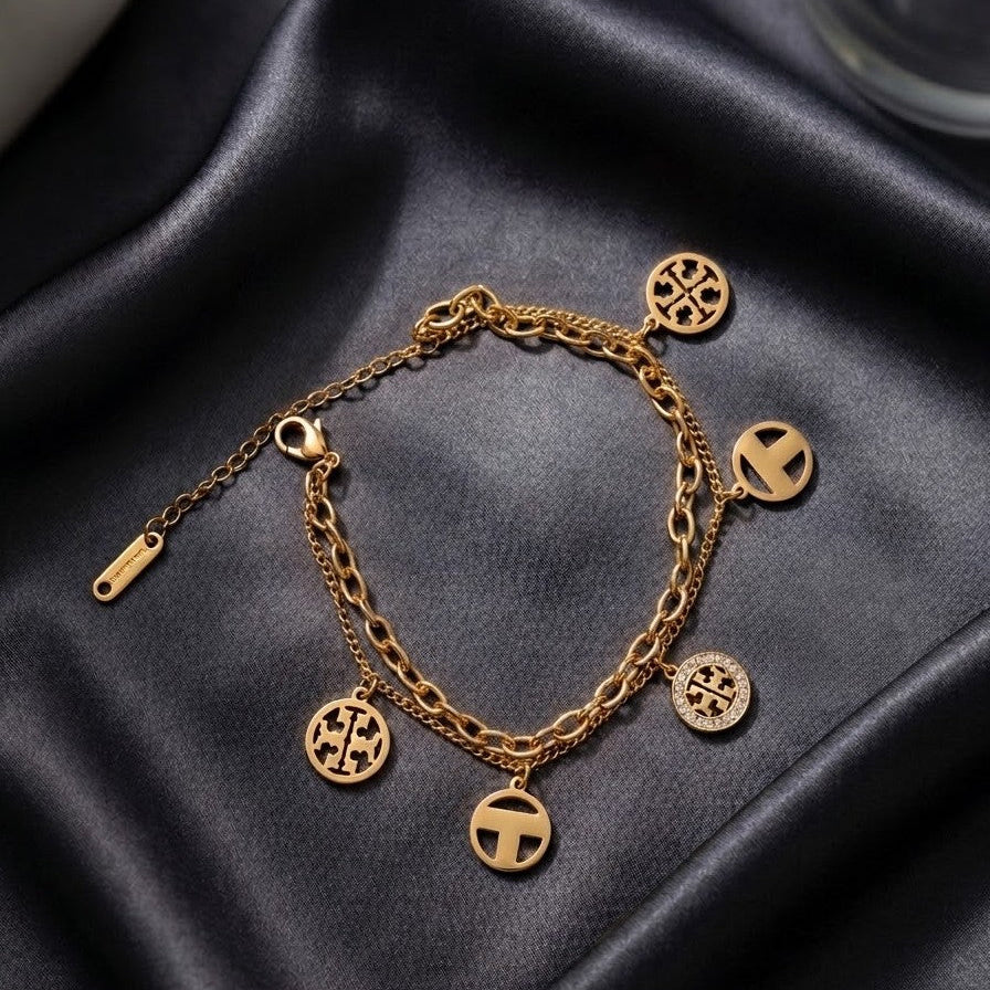 Gold-plated double-layer bracelet with a link chain and five circular cutout charms, including one with crystal accents, displayed on dark grey satin.