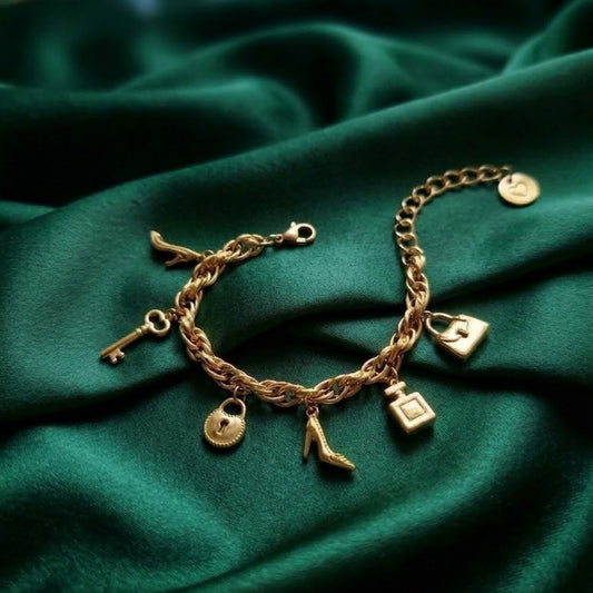 Gold-plated twisted rope chain charm bracelet with a perfume bottle, high heel, handbag, and heart lock charms on emerald green silk.