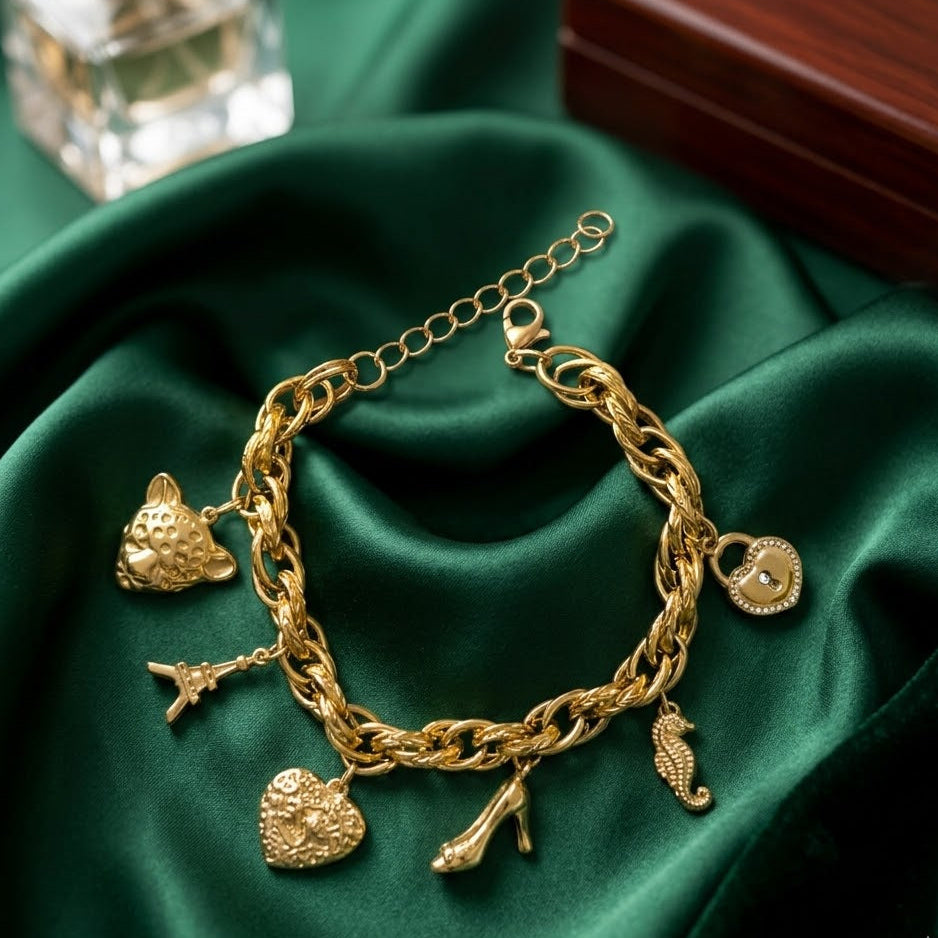 Gold-plated twisted link charm bracelet featuring an Eiffel Tower, panther head, seahorse, and crystal heart lock charms on emerald green silk.