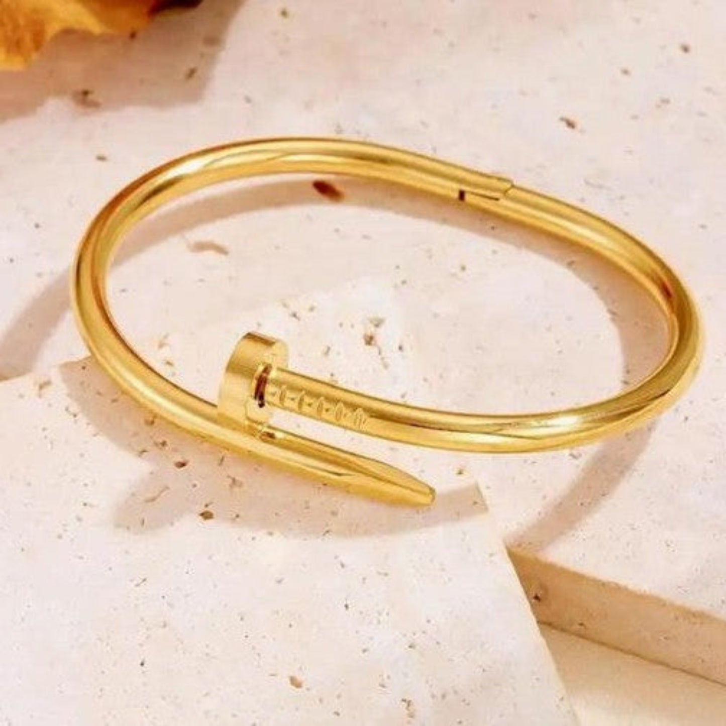 Luxury gold-plated nail-shaped cuff bracelet for women, elegantly draped over white satin silk fabric for a high-end fashion jewelry aesthetic
