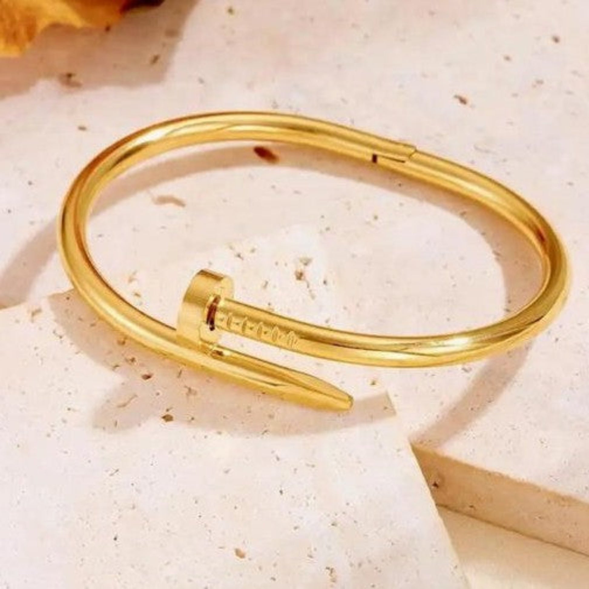 Luxury gold-plated nail-shaped cuff bracelet for women, elegantly draped over white satin silk fabric for a high-end fashion jewelry aesthetic