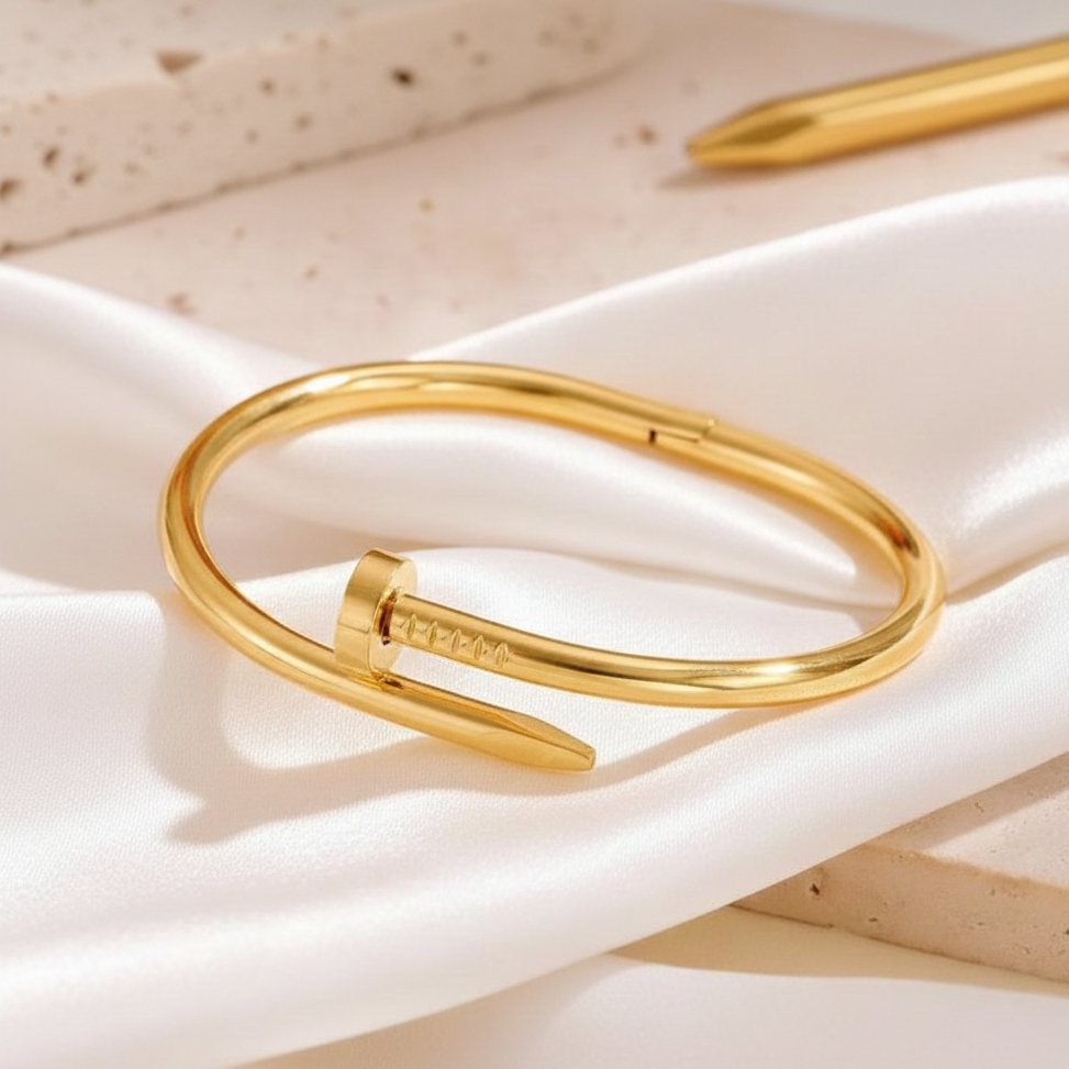 Minimalist gold-plated nail bangle with a polished finish and engraved screw head detail, displayed on a textured beige stone surface with soft natural shadows.