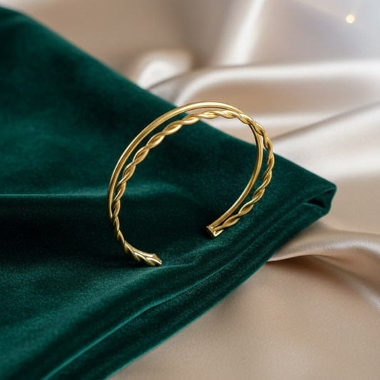 A gold-plated double-layer twisted rope cuff bracelet displayed on a dark emerald green velvet and champagne silk fabric background, highlighting its elegant textured design.