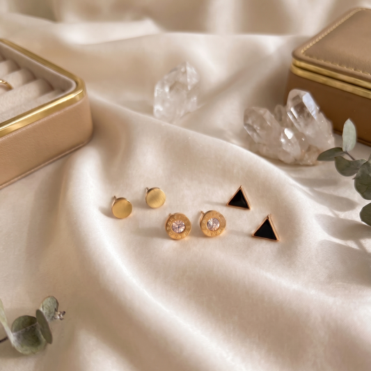 Minimal gold stud earrings set with matte round, crystal center, and black triangle geometric designs on satin background
