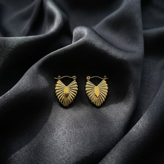 Pair of textured gold fan leaf hoop earrings with a sunburst ribbed design resting on a draped charcoal grey silk background.