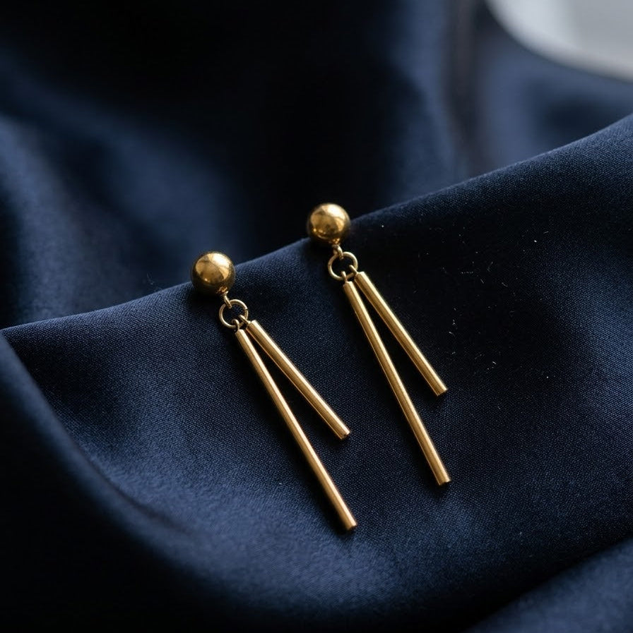 Pair of minimalist gold bar drop earrings with two dangling vertical bars attached to a gold ball stud on dark navy blue silk fabric
