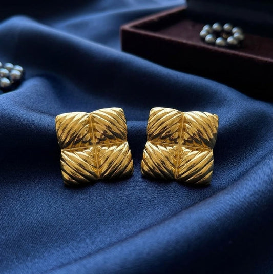 Pair of large gold-plated square stud earrings with a four-way ribbed texture resting on draped royal blue satin fabric