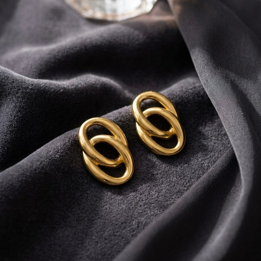 Pair of chunky gold-plated interlocking double oval link statement earrings resting on draped charcoal grey velvet fabric