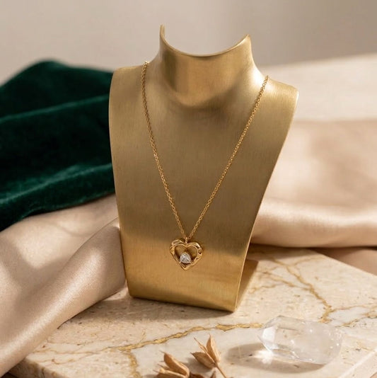 Gold-plated textured heart pendant necklace with a pear-shaped white zircon stone in the center, displayed on white silk fabric with rose petals.