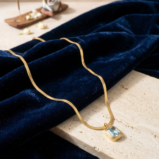 Discover our Gold Herringbone Necklace featuring a regal emerald-cut stone. Perfect for modern layering or as a bold, minimalist statement piece.