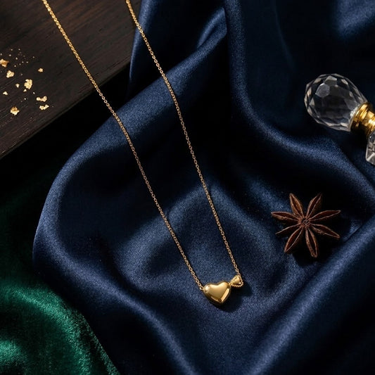 Dainty gold necklace with two heart pendants—one puffed and one small textured heart—resting on dark blue and emerald green silk fabric.