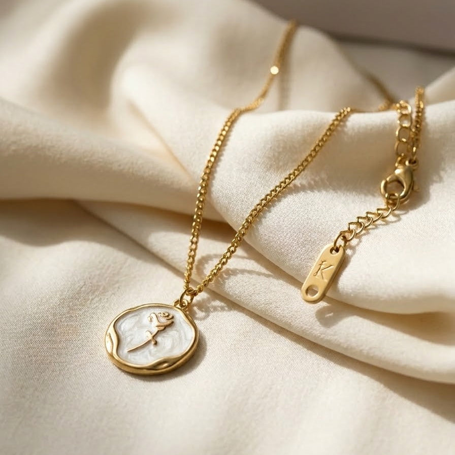 Vintage-style gold coin necklace with a rose relief on a white mother-of-pearl center, resting on a natural stone and silk background.