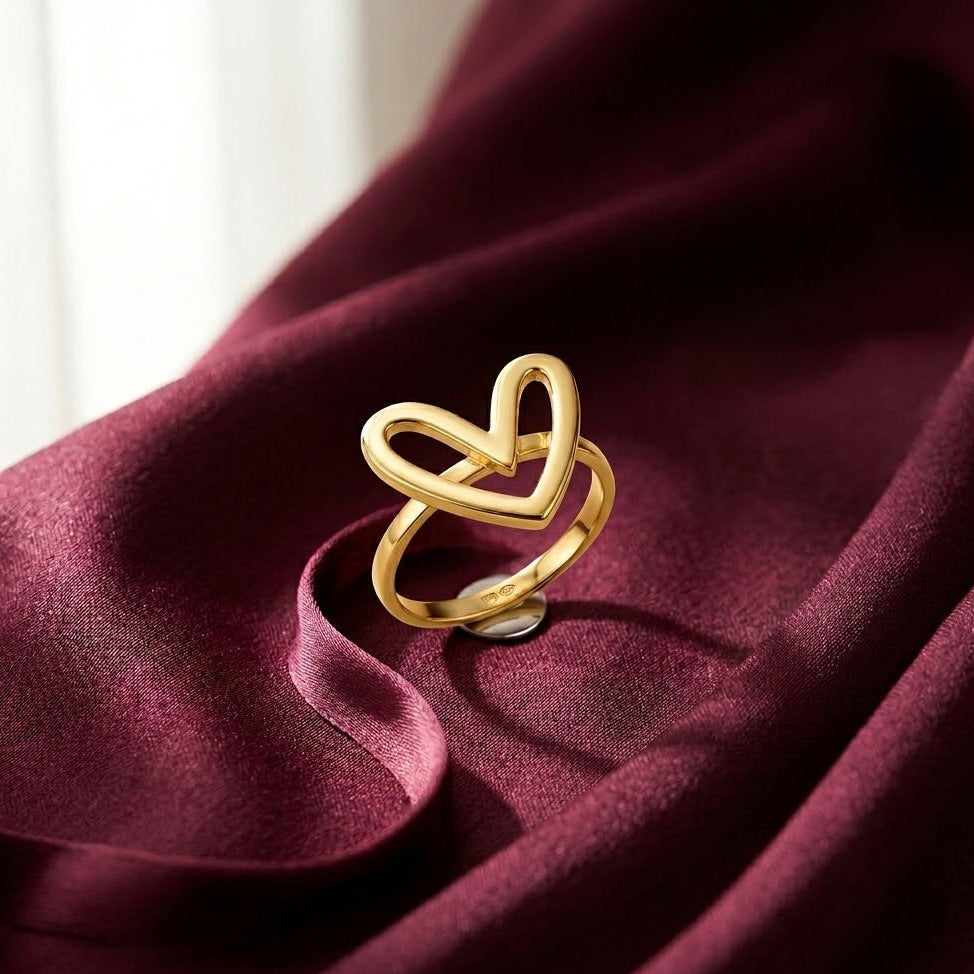 Dainty gold-plated ring with a modern open heart silhouette design, displayed on rich burgundy satin fabric.